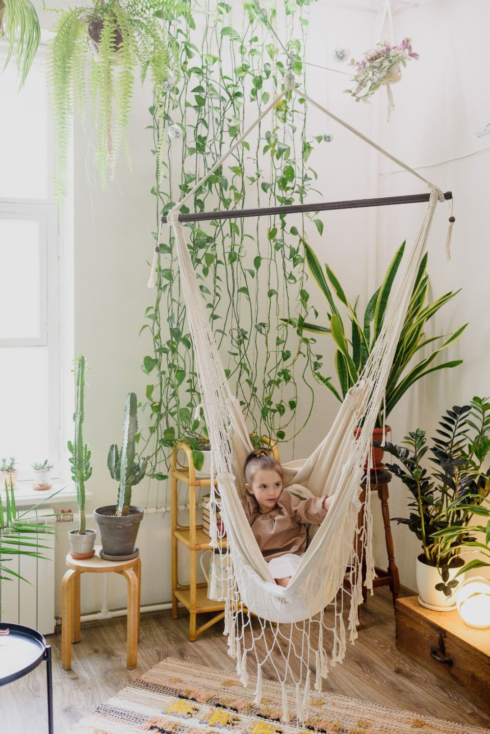 niña descansando en hamaca de interior rodeada de plantas y luz natural